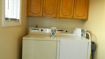 A laundry area with two stacked washers and dryers, wooden cabinets above, and a window with blinds.