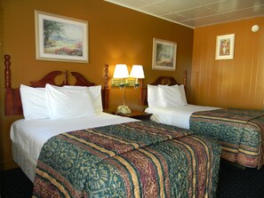 Two single beds with white linens and decorative headboards, accompanied by a nightstand with a lamp and telephone.