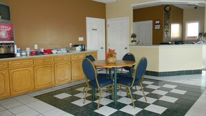A hotel kitchen with a checkered floor, a wooden counter, and blue chairs around a small table. - Fairfax Motel (Roanoke Rapids)