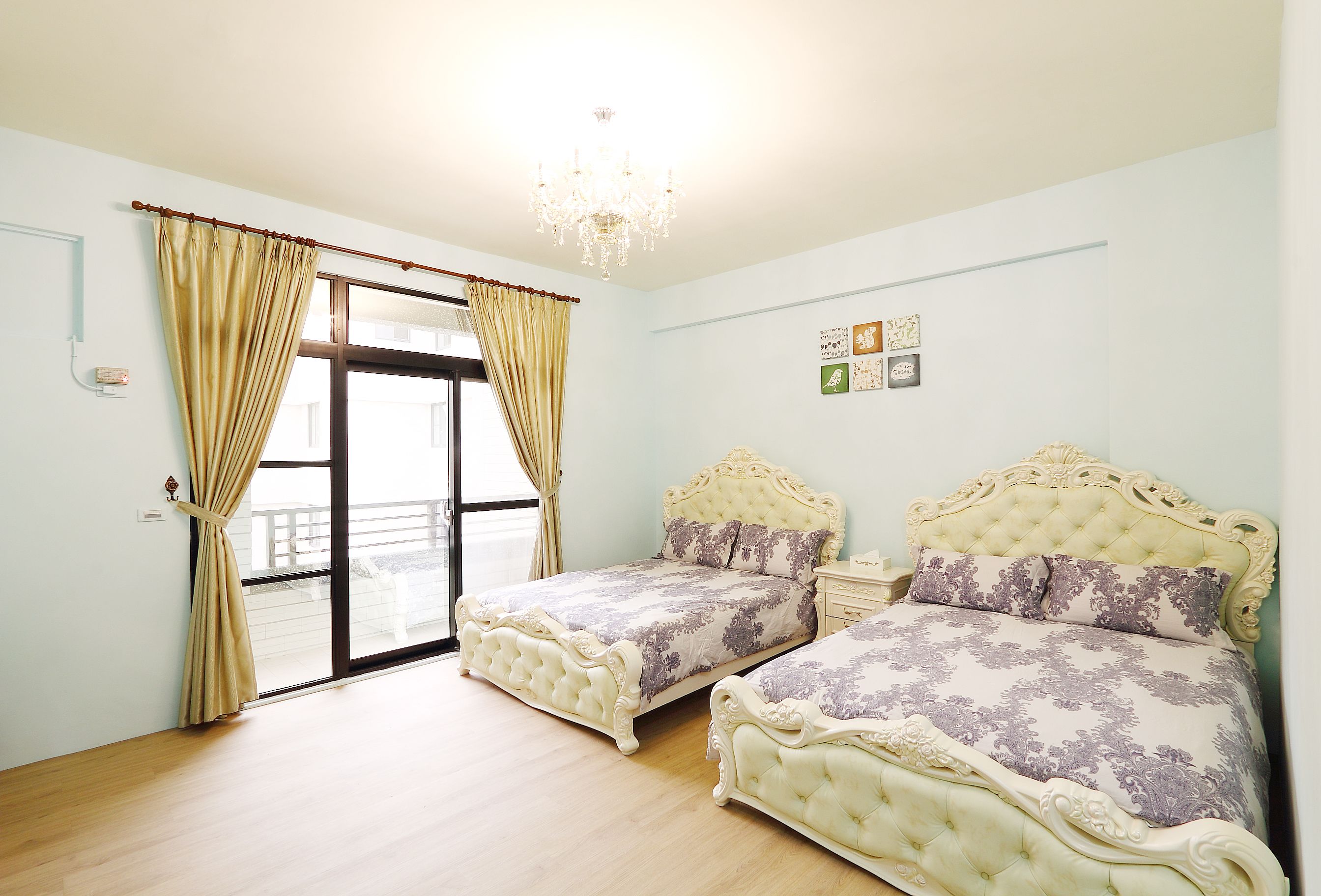 A bedroom with two beds, a chandelier, and a view through a glass door.