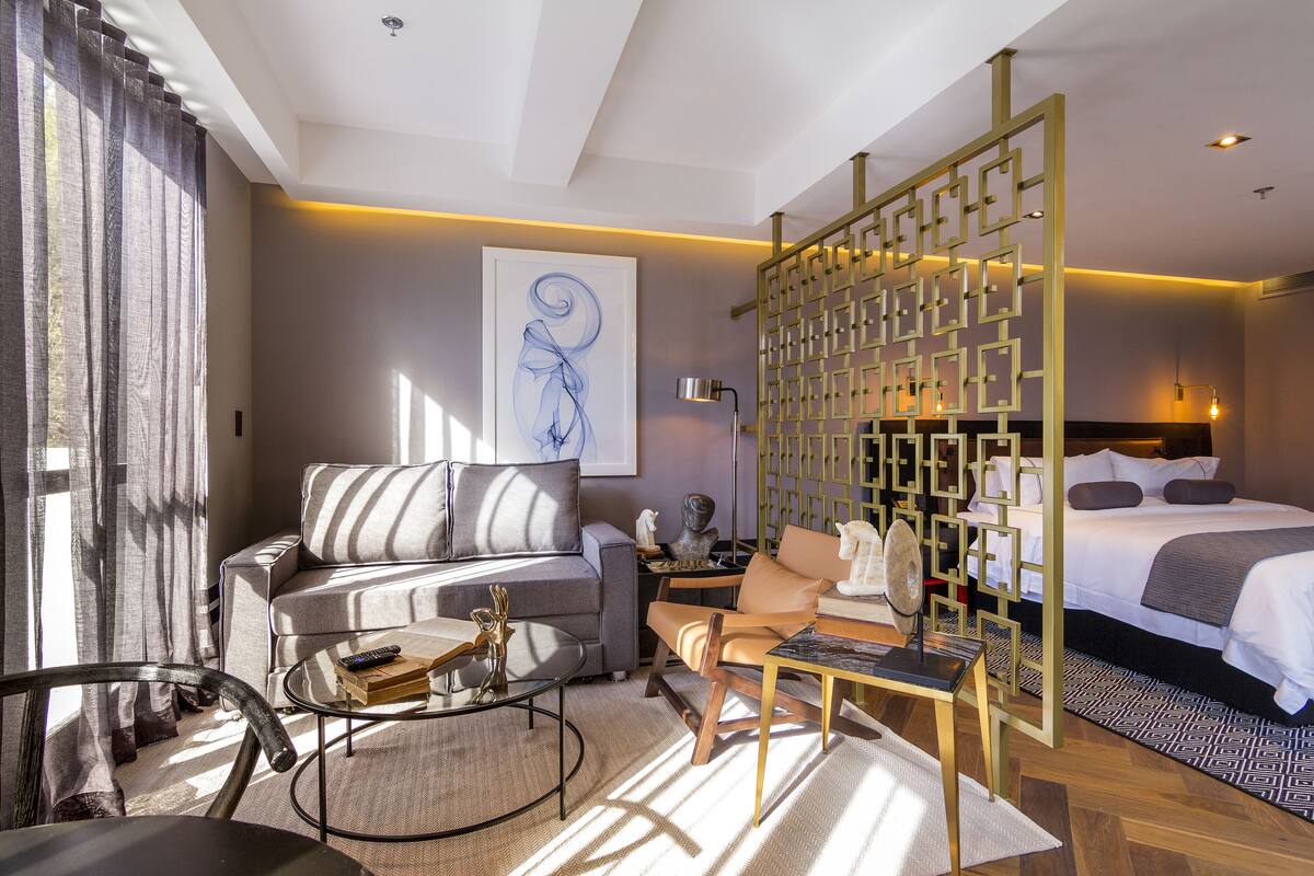 Una habitación de hotel moderna con sofá, sillón, mesa de centro y una cama con cabecero.