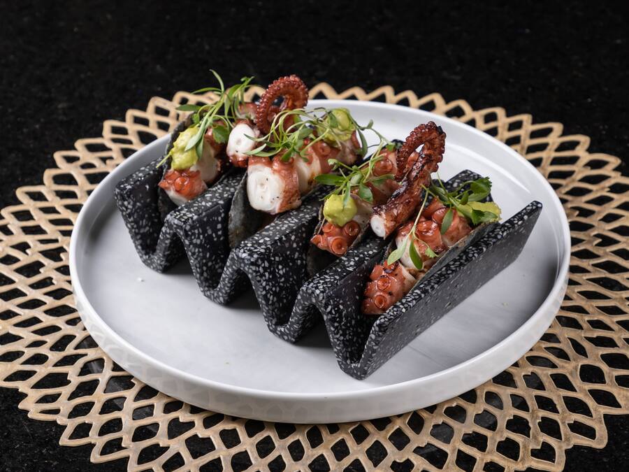 Un plato de sushi de pulpo con adornos sobre una vajilla blanca.