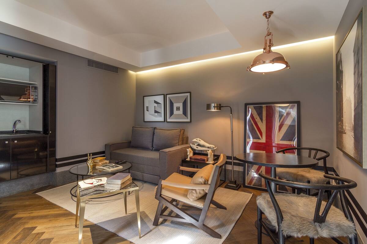 Una sala de estar moderna con un sofá, una mesa de centro, una silla y una mesa de comedor. Hay un espejo, un marco de fotos y una lámpara.