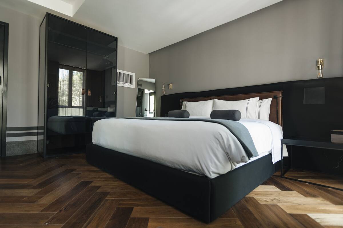 Un dormitorio moderno con una cama grande, cabecera oscura y suelo de madera.