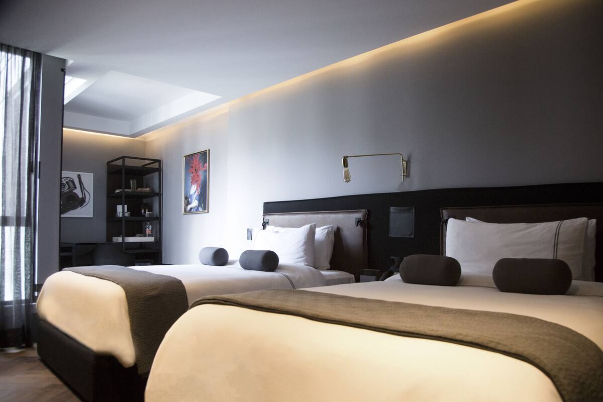 Habitación de hotel con dos camas, una estantería, un cuadro y un tragaluz.