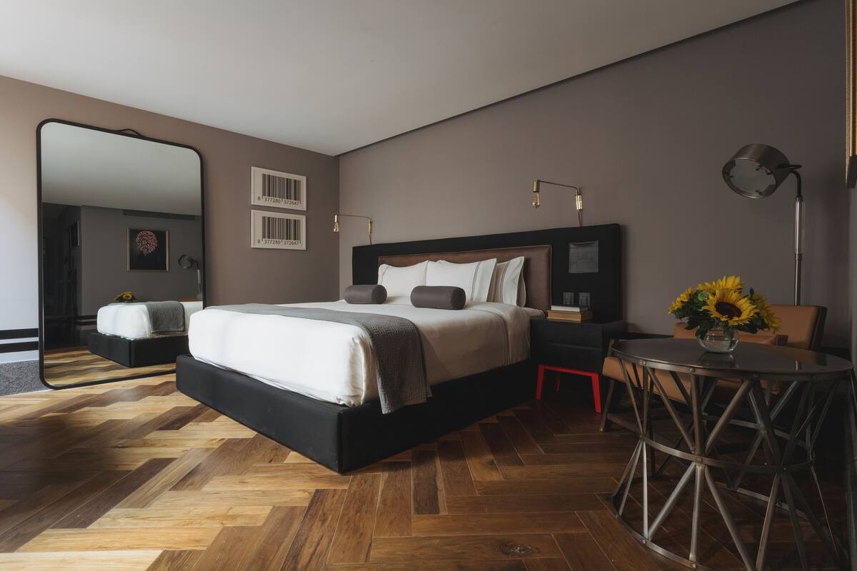 Un dormitorio moderno con una cama grande, una mesa redonda para comer y un espejo.