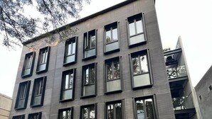 Eine Person fährt Fahrrad vor einem modernen Gebäude mit vielen Fenstern und einer glatten Fassade.