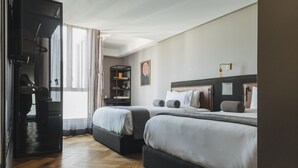 Ein Hotelzimmer mit zwei Betten, einem Kleiderschrank, einem Schreibtisch und einem großen Fenster mit Vorhängen.