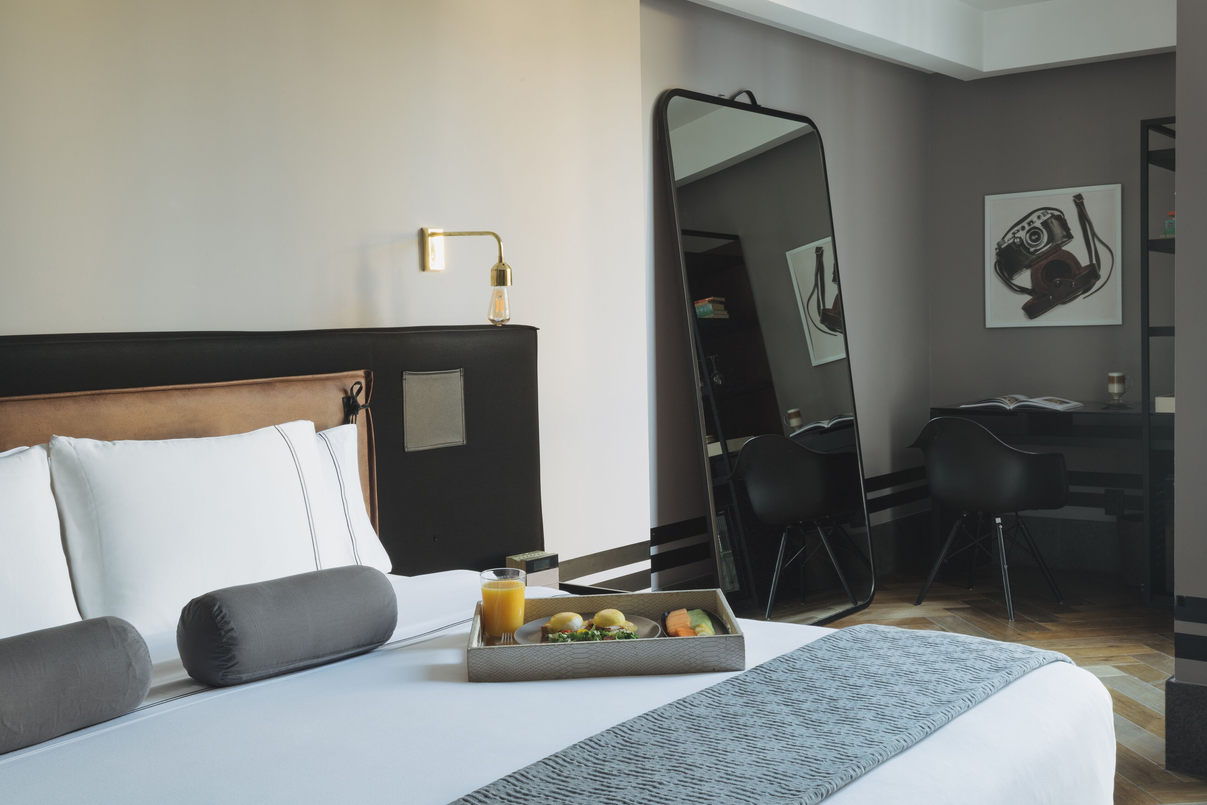 Una habitación de hotel con una cama bien hecha, una bandeja de desayuno, un escritorio y un espejo grande.