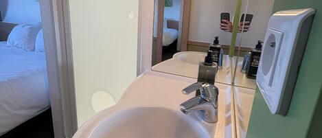 A hotel bathroom with a sink, mirror, and toiletries.