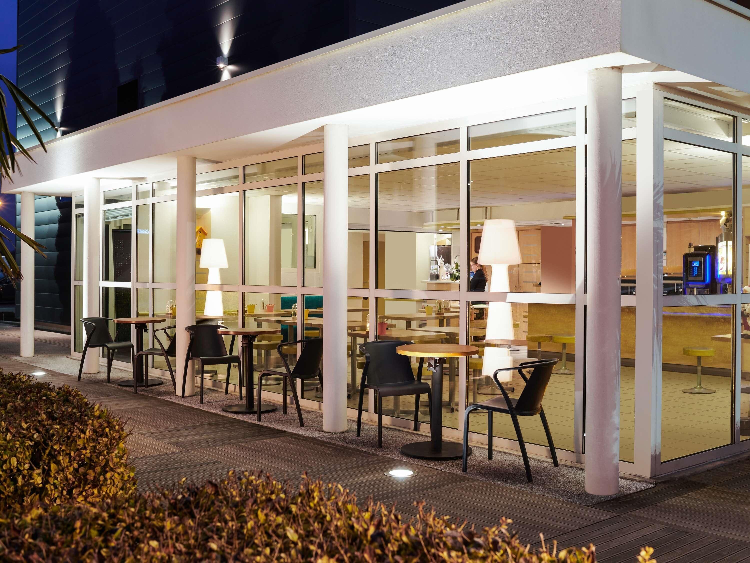 An outdoor seating area with tables and chairs, a glass wall, and a building in the background.