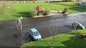 Uma área de estacionamento com um carro azul, um pequeno edifício e um campo gramado ao fundo.