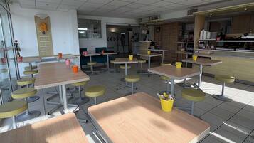 A clean, modern cafeteria with multiple tables and chairs, a clock on the wall, and a counter with food items.
