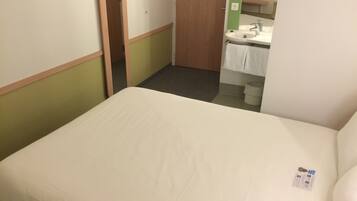 Una stanza piccola e pulita con un letto singolo, una porta di legno, un lavandino e uno specchio.