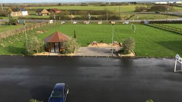 Un espace de stationnement avec une voiture bleue, un petit pavillon et un terrain herbeux délimité par une clôture.