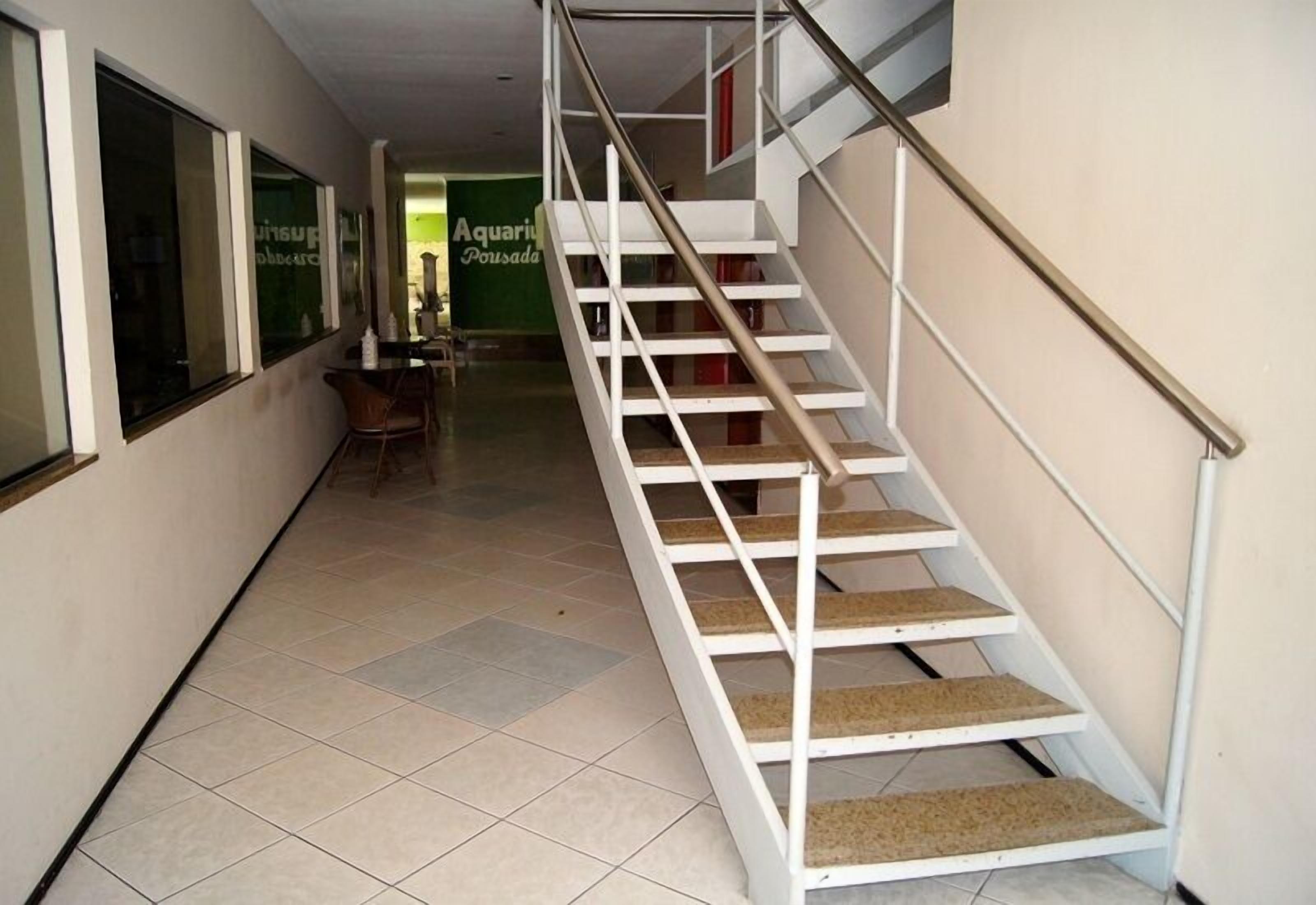 A staircase with white railings and carpeted steps leading to a room with a green wall and a sign that reads "Aquarium Pousada".