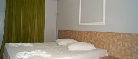 Una cama bien hecha con sábanas y almohadas blancas, un cabecero de madera, una mesita de noche de madera y una cortina verde.