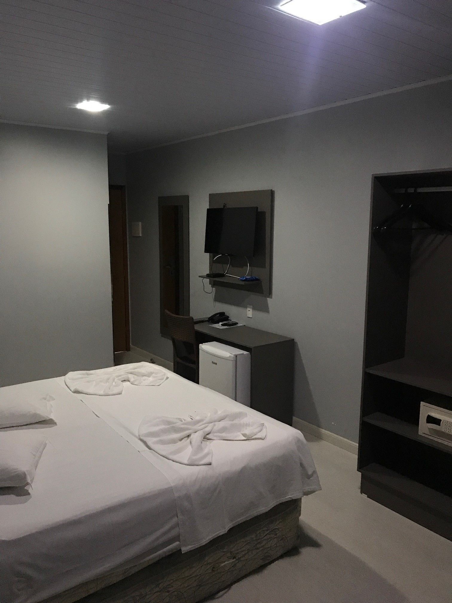 A hotel room with a bed, a desk with a computer, a TV, and a wardrobe.