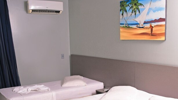 Een hotelkamer met twee bedden, een schilderij van een strandgezicht, een airconditioning en een handdoekrek.