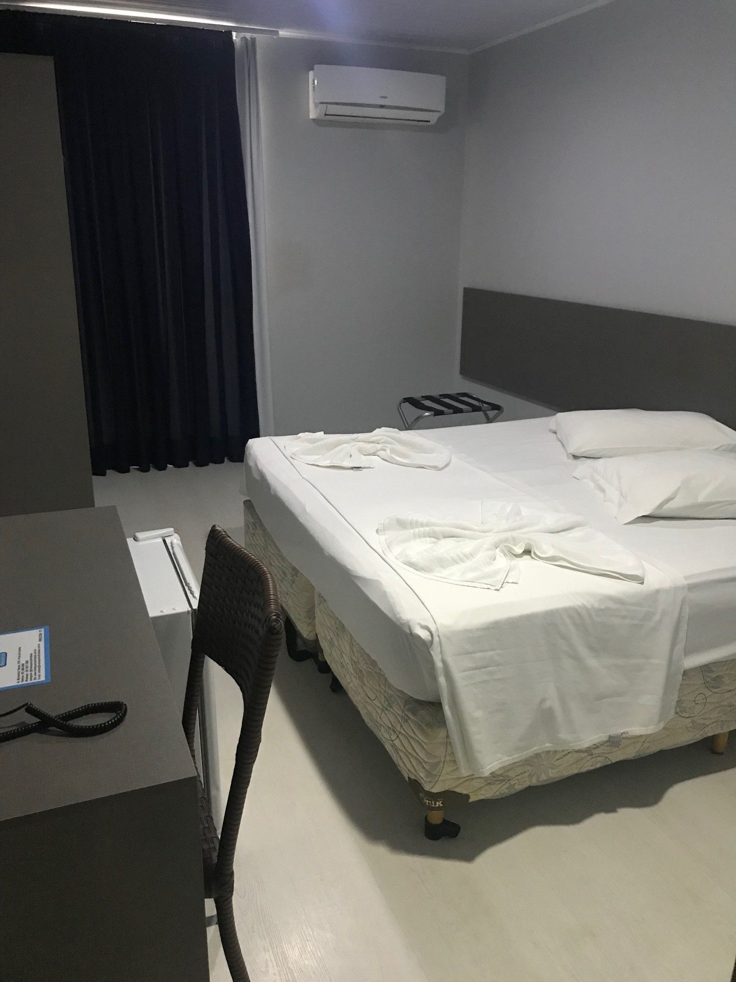 Habitación de hotel con cama, escritorio, silla, aire acondicionado y cortina.