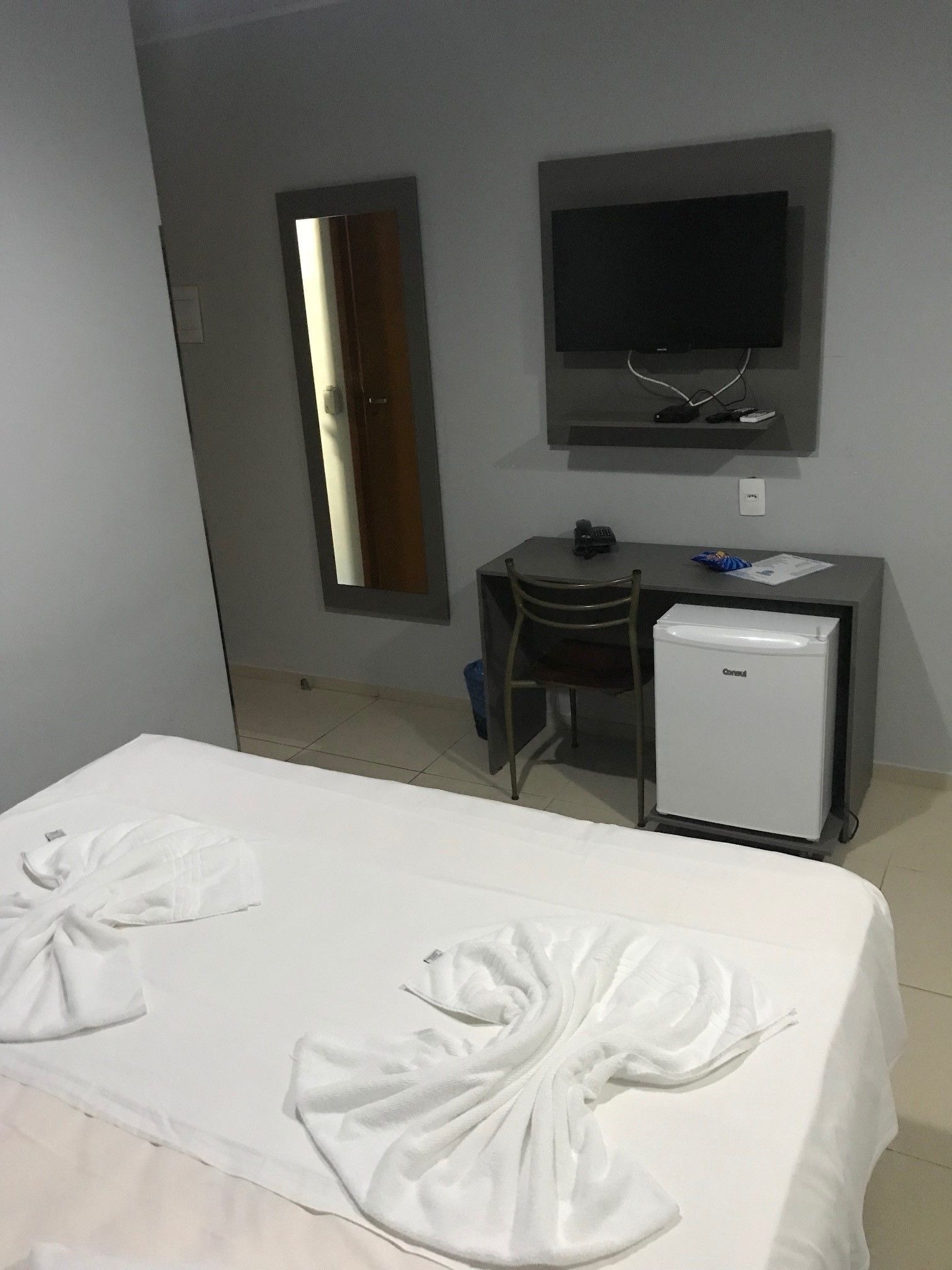 Une chambre d’hôtel équipée d’un lit, d’un bureau, d’une télévision et d’un petit réfrigérateur.