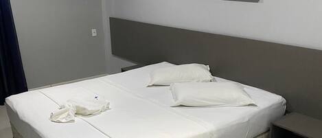 A neatly made bed with white linens, a headboard, and a small bedside table.