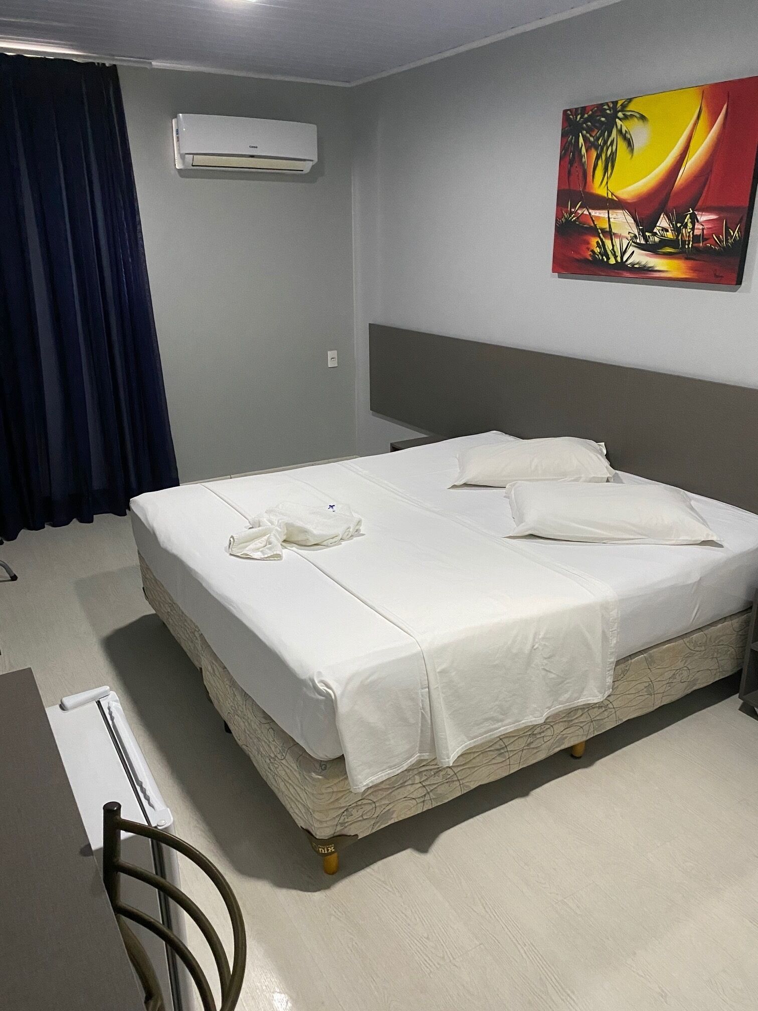 Habitación de hotel con cama, aire acondicionado, un cuadro y cortina.