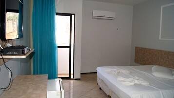 Quarto de hotel com uma cama, uma escrivaninha com telefone, uma televisão na parede e um aparelho de ar condicionado.