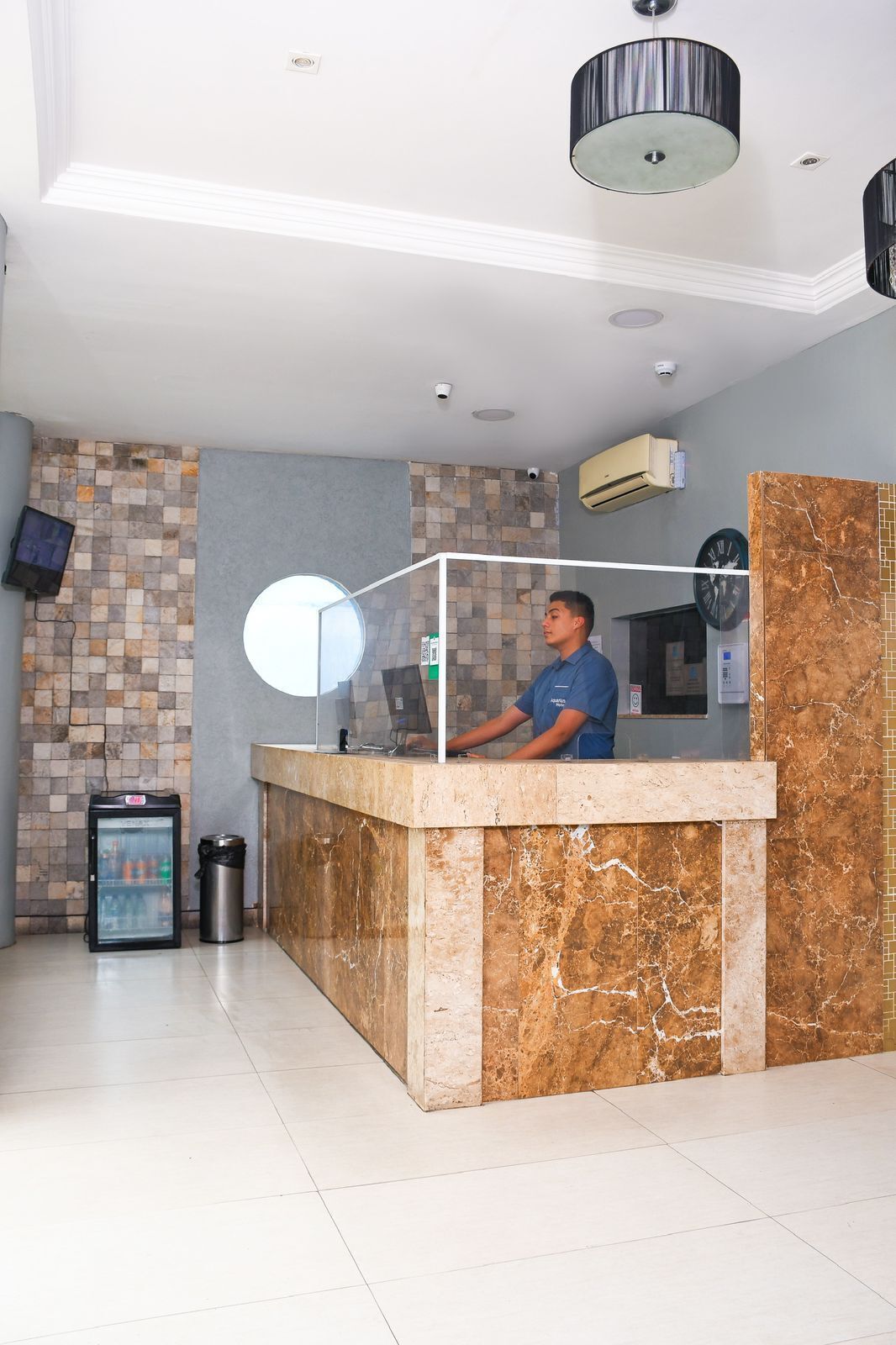 A reception desk with a marble counter, a digital screen, and a clock on the wall.
