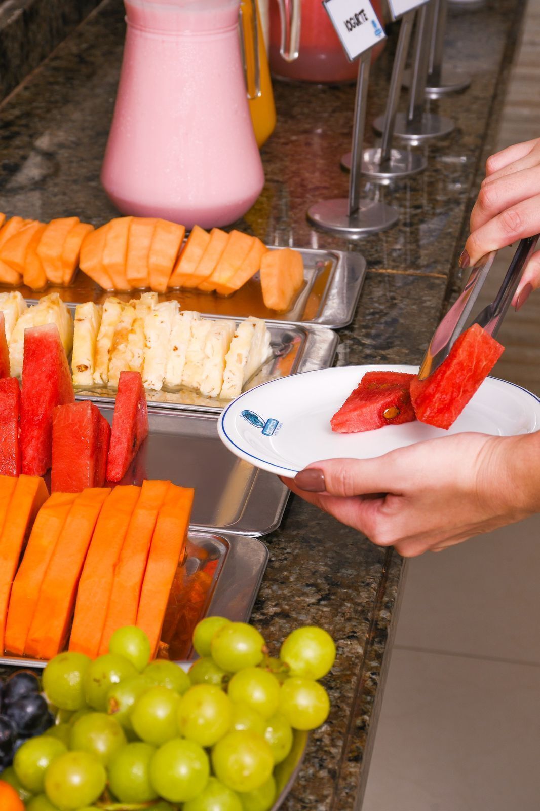 Een buffet met verschillende soorten fruit en een dispenser voor roze drank.