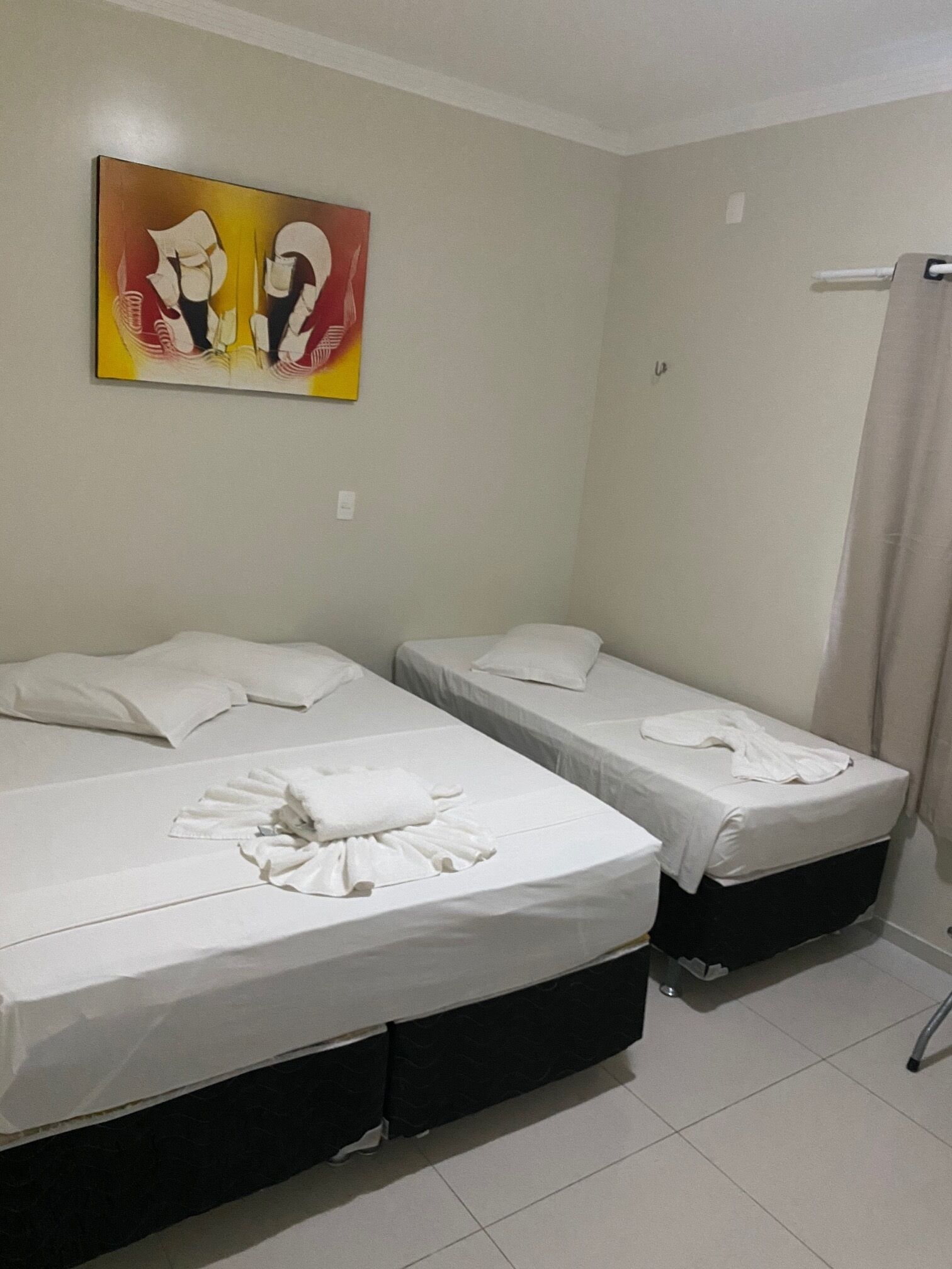 A hotel room with two beds, a painting on the wall, and a shower curtain.