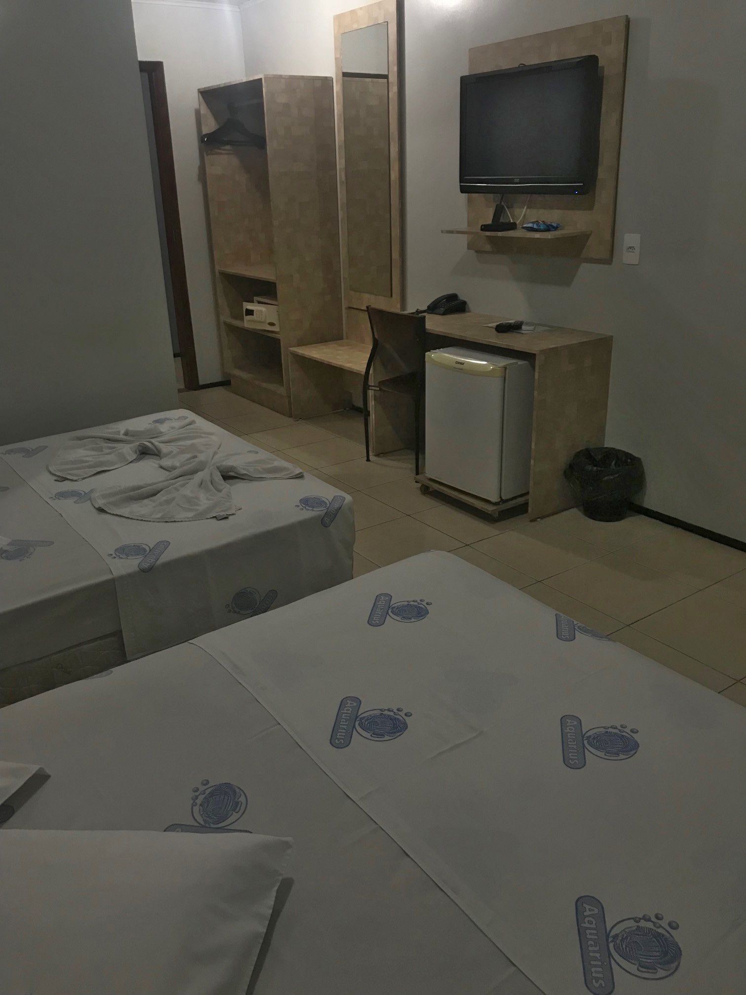 Ein Hotelzimmer mit zwei Betten, einem Schreibtisch, einem Stuhl, einem Fernseher und einem kleinen Kühlschrank.