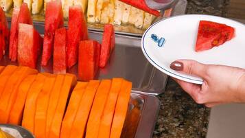 Un bufé con diversas frutas y verduras, entre ellas sandía, piña y uvas.