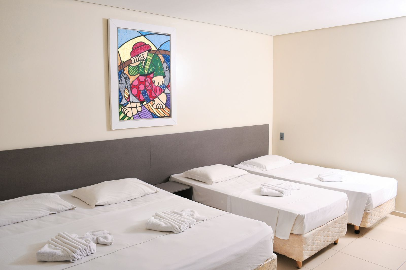 A hotel room with two single beds, white linens, and neatly folded towels. A colorful artwork is displayed on the wall above the beds.