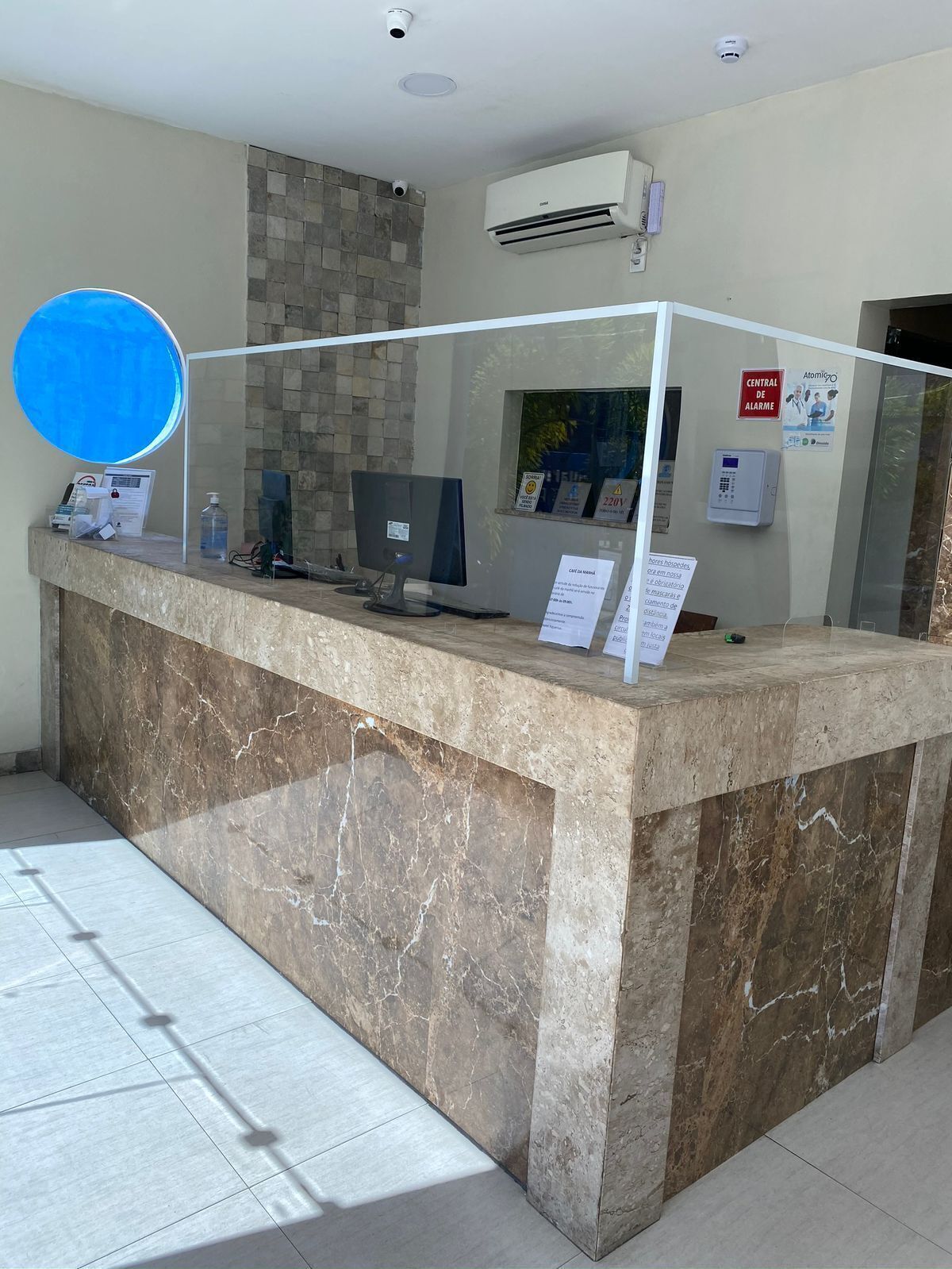 Um balcão de recepção com bancada de mármore, um computador e uma divisória de vidro.