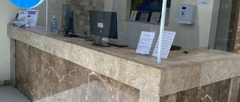 Um balcão de recepção com bancada de mármore, um computador e uma divisória de vidro.