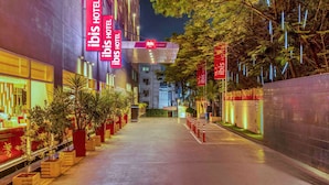 Vue nocturne de l’hôtel Ibis, avec son enseigne illuminée et un chemin bordé de plantes en pot.