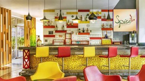 L’intérieur d’un restaurant, avec un coin bar, des chaises rouges et jaunes, et diverses bouteilles exposées sur des étagères.