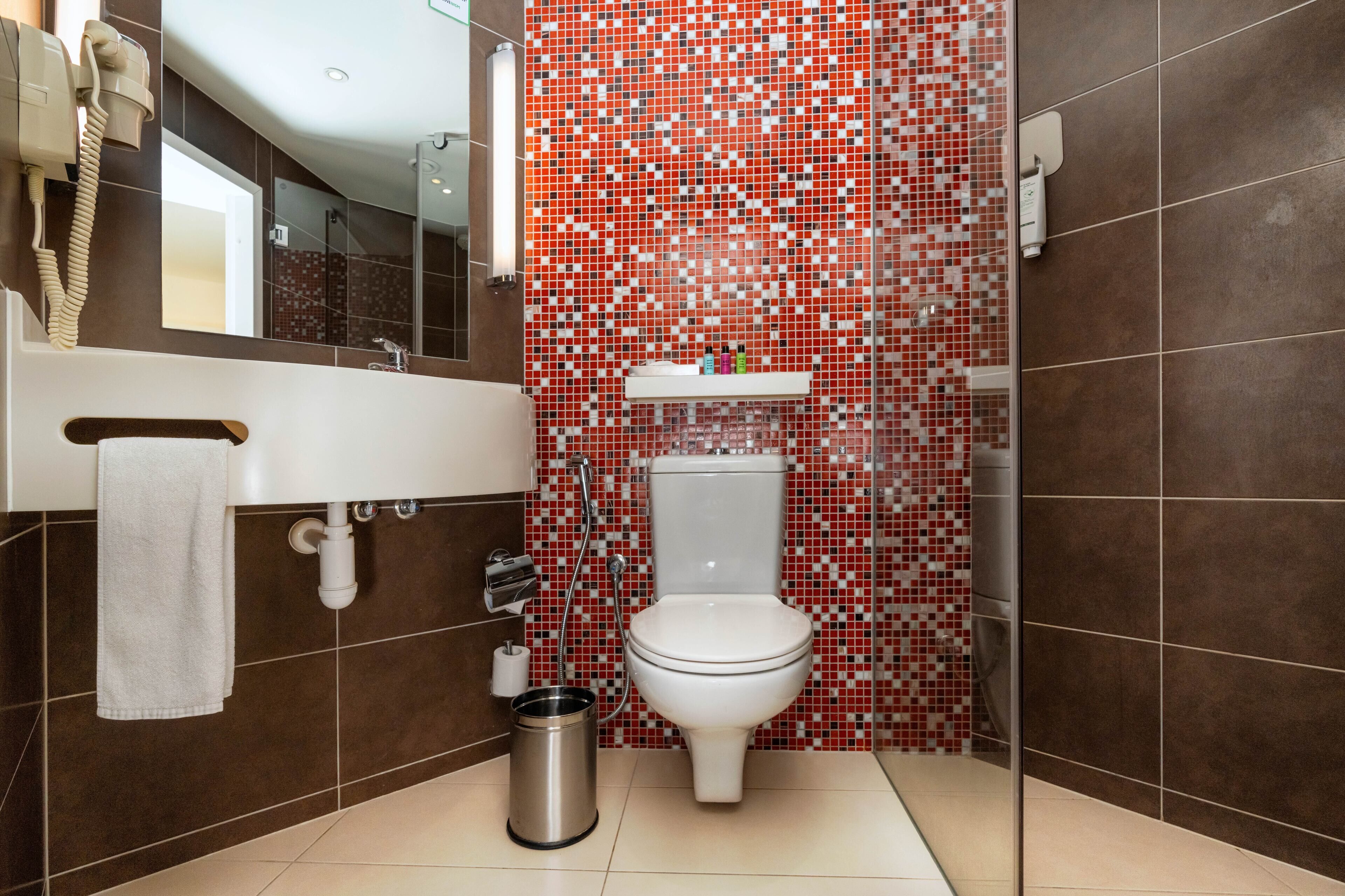 A bathroom with a white toilet, a sink with a towel, and a trash can.