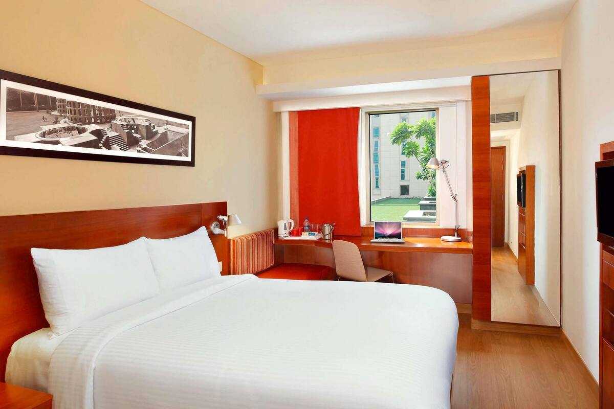 Habitación de hotel con cama, escritorio, silla y un ventanal con vistas.