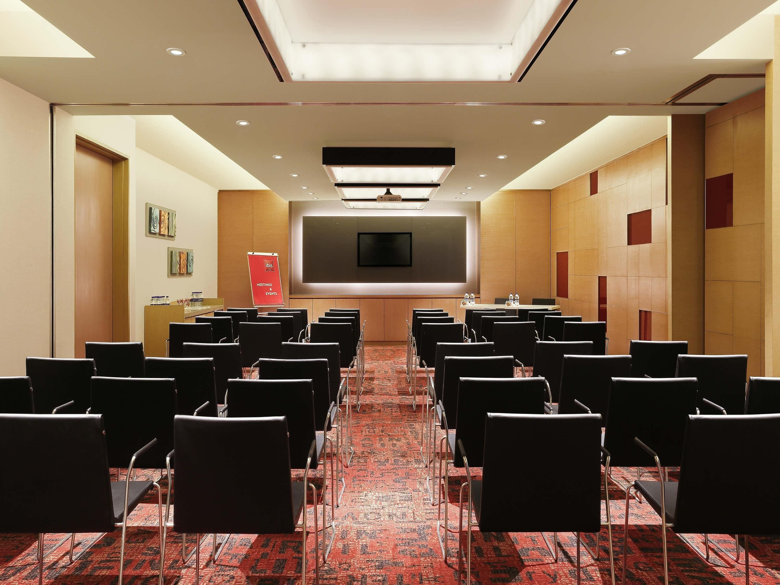 A conference room with rows of chairs, a large screen, and a podium.