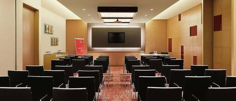 A conference room with rows of chairs, a large screen, and a podium.