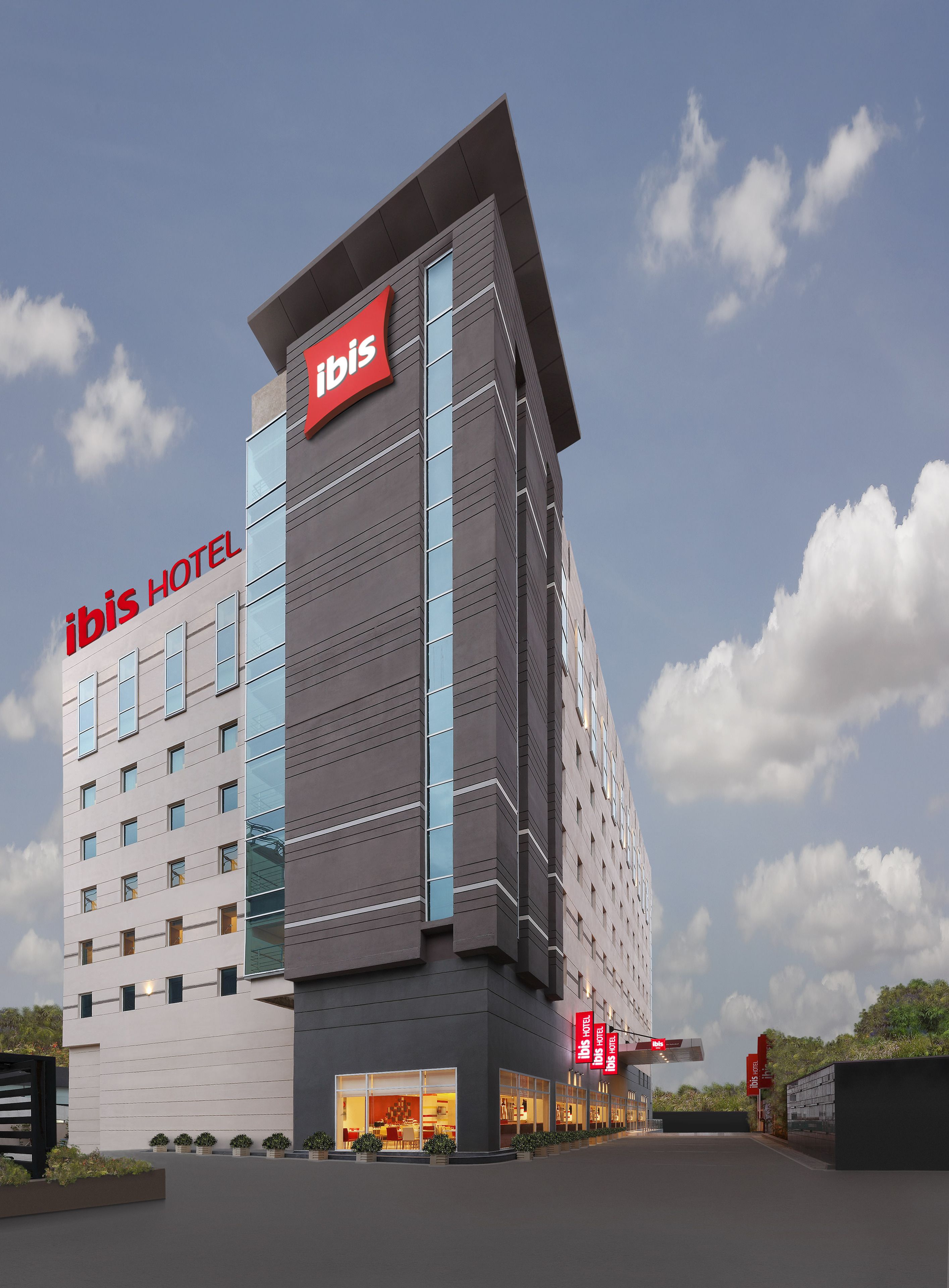 A modern hotel building with a prominent "ibis" sign, multiple windows, and a well-lit entrance.