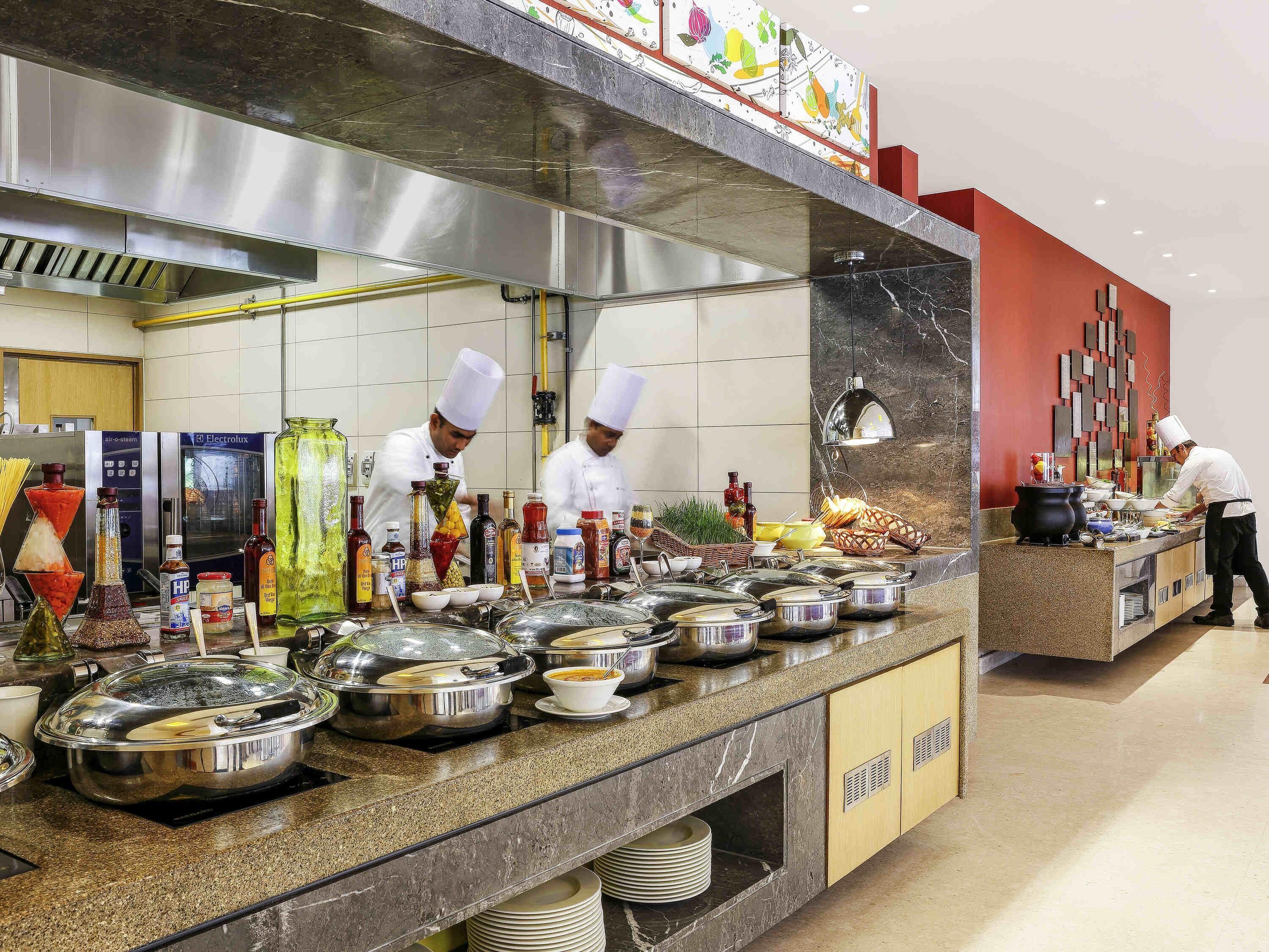 A buffet setup with multiple serving stations, a stainless steel range hood, and a tiled backsplash.