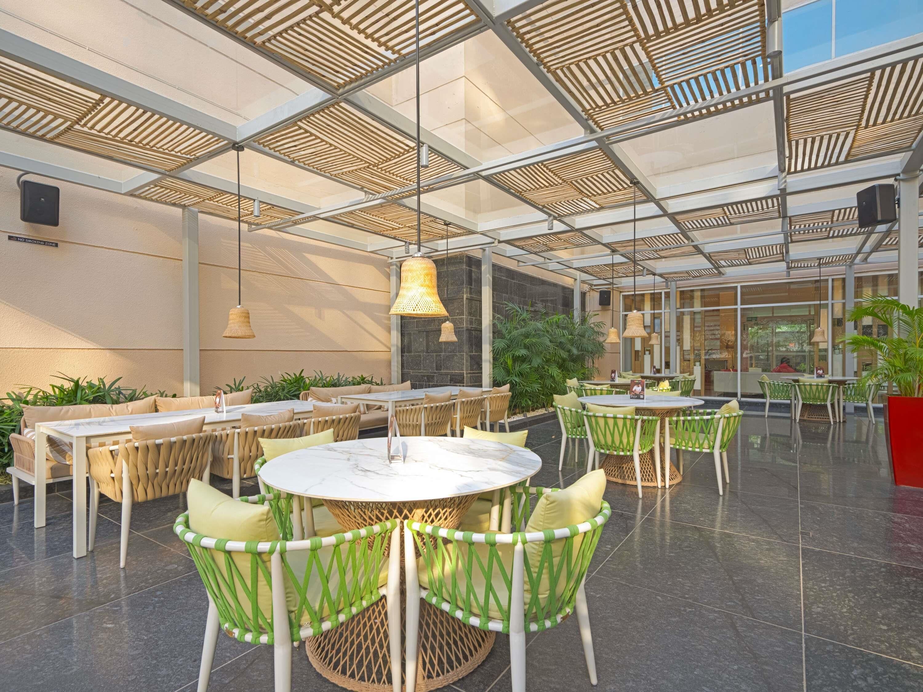 Un espace de restauration en plein air avec des tables et des chaises rondes, un plafond en verre et des plantes en pot.