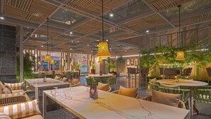 Un espace intérieur moderne, aménagé avec des tables et des chaises, une table surmontée d’un plateau en marbre et des lampes suspendues.