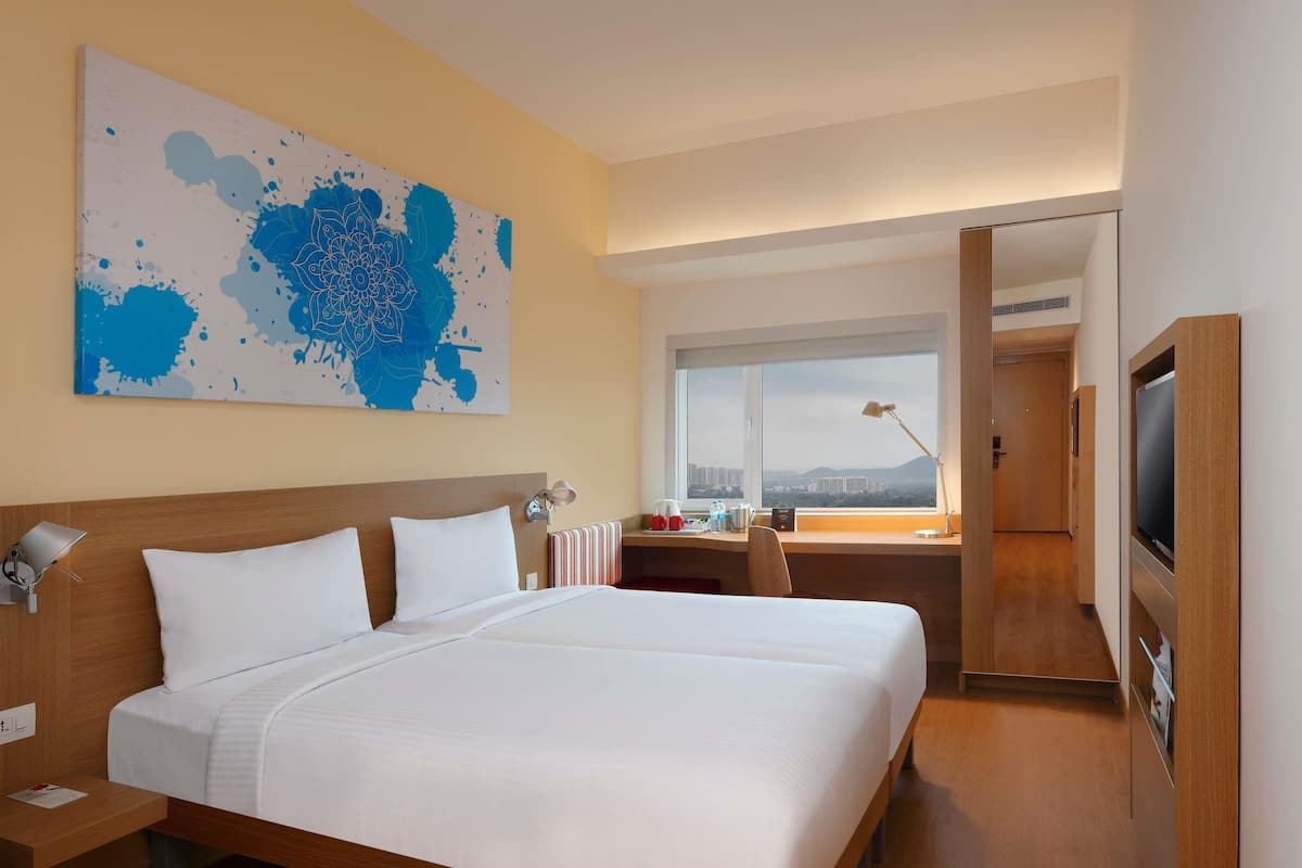 Habitación de hotel con una cama grande, un escritorio con computadora, televisor y ventana con vista a la ciudad.