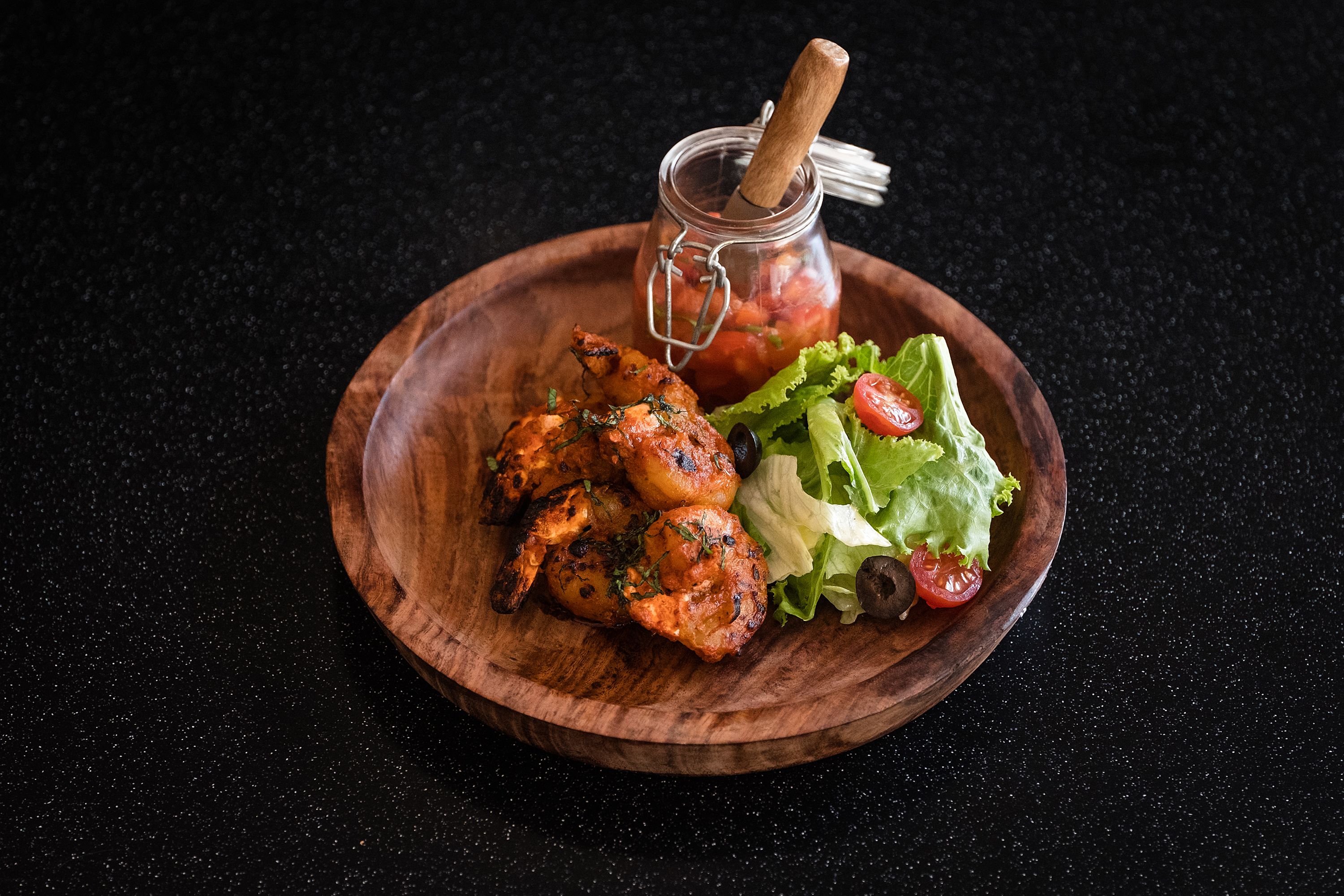 Un piatto di legno con pollo alla griglia, un'insalata e un vasetto di salsa.