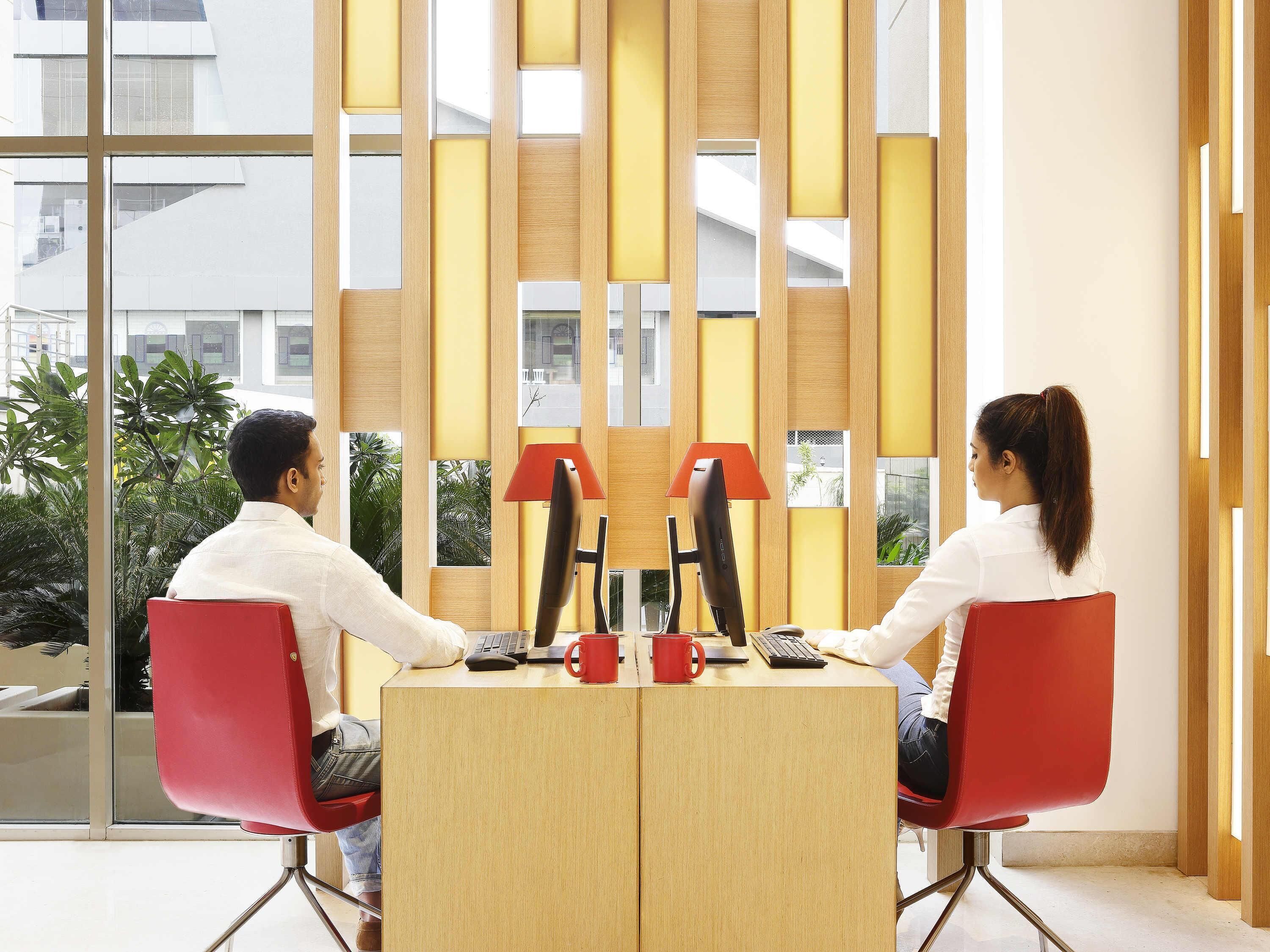 A modern office with two red chairs, a wooden desk, and a view of greenery outside.