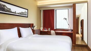 Habitación de hotel con una cama grande, un escritorio, una silla, una lámpara de escritorio, una ventana con cortinas rojas y un cuadro en la pared.